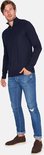 Man met donkerblauwe trui met rits tot de borst, jeans en bruine schoenen.