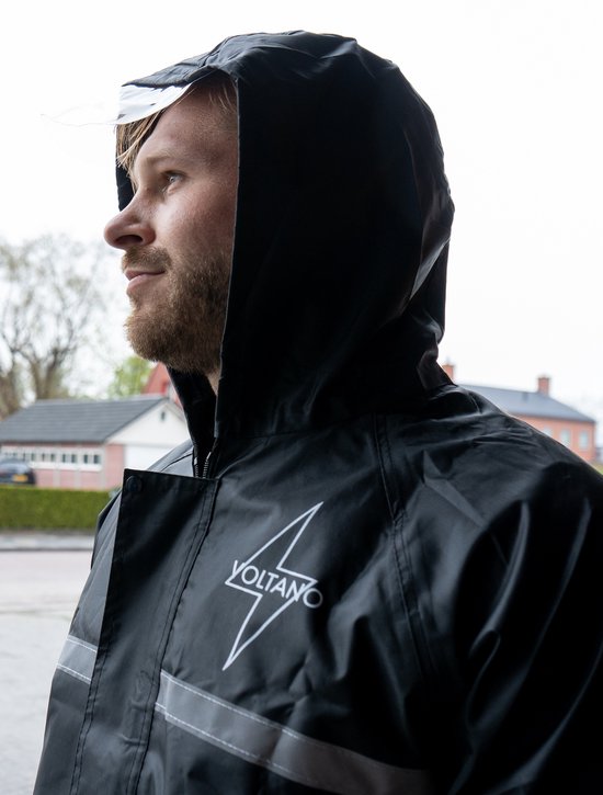 Profiel van een man in de regen, die een zwarte regenjas met capuchon en reflecterende strepen draagt. De jas heeft het "VOLTANO" logo.