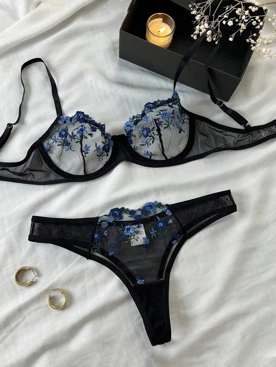 Zwarte kanten BH en string set, versierd met blauwe bloemen. Zwarte doos met brandende kaars.