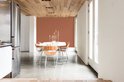 Eetkamer met terracotta muur, houten plafond en oranje stoelen.