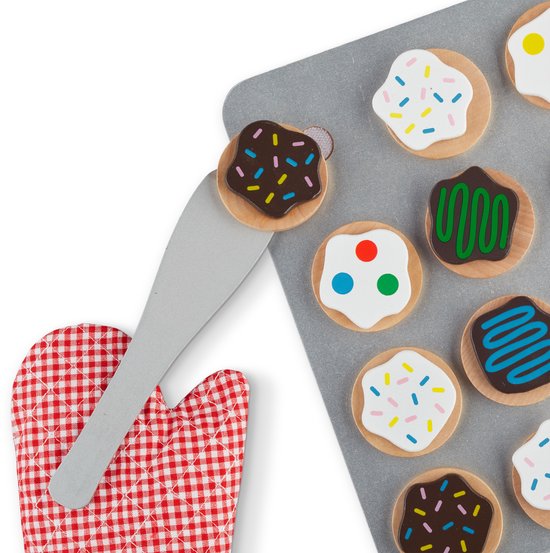 Close-up van houten koekjes op bakplaat met rode ovenwant en spatel. Koekjes met witte icing, sprinkles, groene en blauwe icing, chocolade en polka dots.