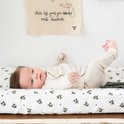 Baby ligt op een wit verschoonkussen met groen bloemenprintje. Draagt een beige romper en broekje.