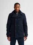 Man met donkerblauwe peacoat met dubbele rij knopen, staande ribkraag en jeans.