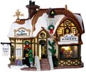 Verlicht Lemax kerstdorp gebouw 'Devaney's Bakery' met 'Ye Olde Tea Shoppe' uithangbord, besneeuwde daken en kerstdecoraties.