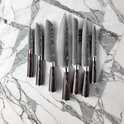 Een set van zeven damascus messen met donkere handvatten, liggend op een marmeren ondergrond.