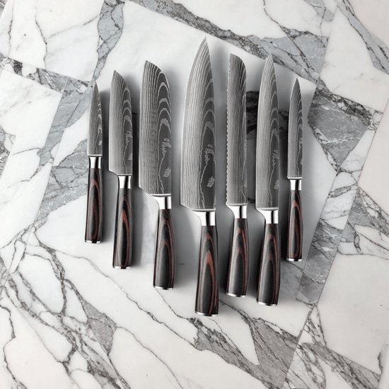 Een set van zeven damascus messen met donkere handvatten, liggend op een marmeren ondergrond.