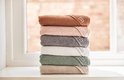Stapel van zes badcapes in verschillende kleuren: bruin, roze, grijs, wit, groen en beige.