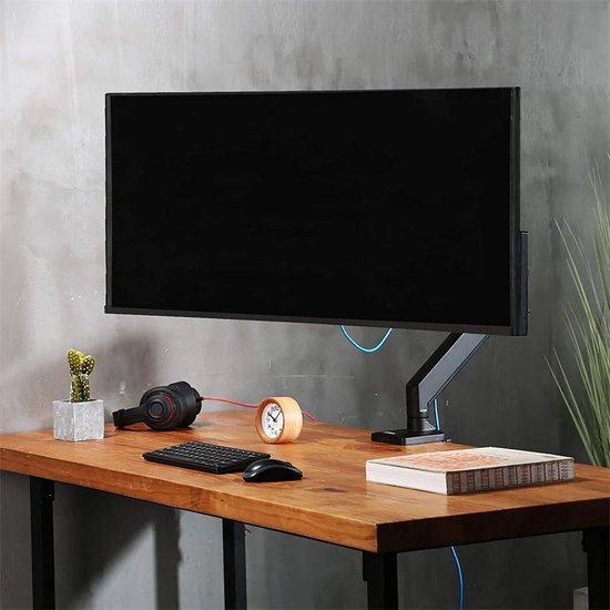 Zwarte VESA monitorbeugel met een gasveer, gemonteerd op een houten bureau, met een monitor, koptelefoon en een kleine cactus.