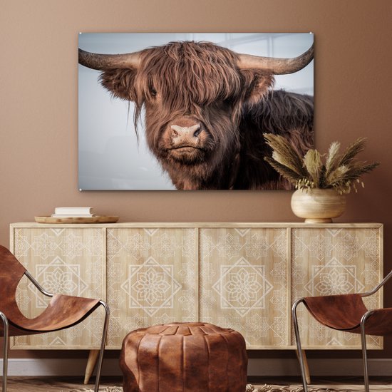 Glasafbeelding van een bruine Schotse hooglander met grote hoorns, hangend boven een dressoir.