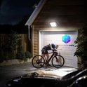 Man op een fiets bij een garage, verlicht door een aan de muur gemonteerde zonnelamp.