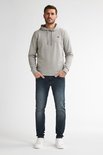 Man in grijze hoodie en donkerblauwe slim fit jeans, witte sneakers.