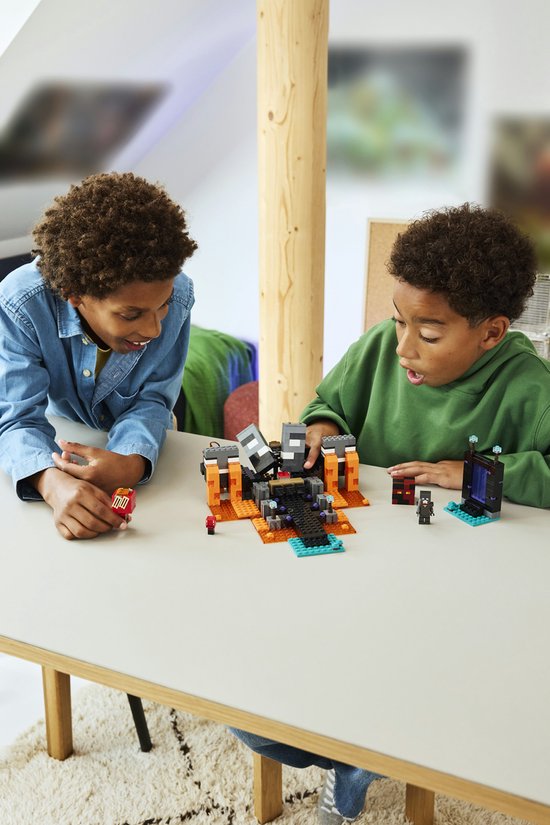 Deux garçons jouent avec un set LEGO Minecraft Wither Battle avec figurines et blocs de construction orange et gris.