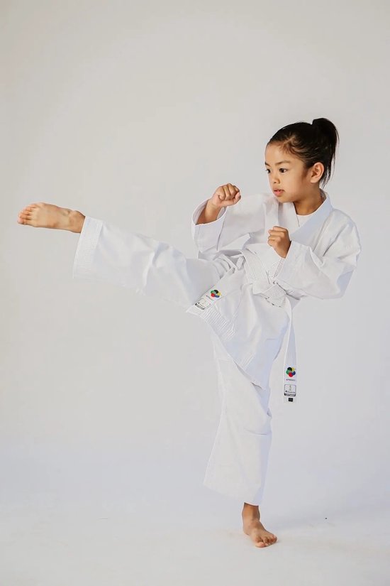Jeune fille en gi de karaté blanc avec ceinture blanche, exécutant un coup de pied haut.