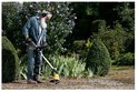 Een oudere man met baard en koptelefoon gebruikt de Kärcher onkruidverwijderaar in de tuin.