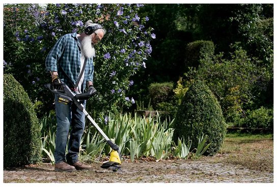 Een oudere man met baard en koptelefoon gebruikt de Kärcher onkruidverwijderaar in de tuin.