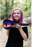 Vrolijke vrouw met paars haar houdt een ukelele vast met een zonsondergangprint. De ukelele heeft blauwe, paarse, oranje en gele kleuren.