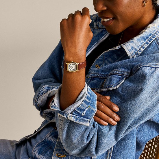 Model met een gouden Fossil horloge met crèmekleurige wijzerplaat en bruin leren bandje om de pols.
