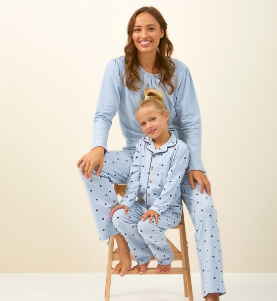 Vrouw en meisje zitten naast elkaar op een trapje, beiden dragen een lichtblauwe pyjama met donkerblauwe hartjesprint en donkerblauwe bies.