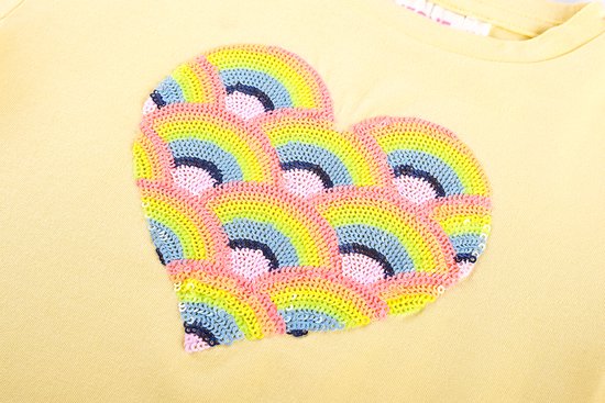 Detail van een lichtgele t-shirt met een hartvormige paillettenprint in regenboogkleuren.