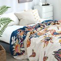 Een sprei met een veelkleurig bloemenpatroon in blauw, roze, geel en oranje, met vlinders en een donkerblauwe rand.