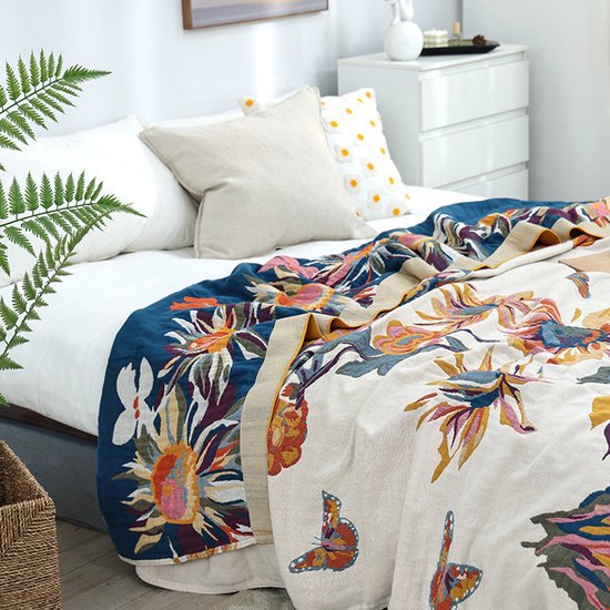 Een sprei met een veelkleurig bloemenpatroon in blauw, roze, geel en oranje, met vlinders en een donkerblauwe rand.