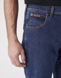 Sluiting van een spijkerblauwe Wrangler spijkerbroek met bruine naden en een bruin leren label.
