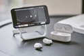 Witte Belkin oordopjes en oplaadcase naast een smartphone op een telefoonstandaard.