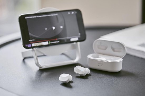 Witte Belkin oordopjes en oplaadcase naast een smartphone op een telefoonstandaard.