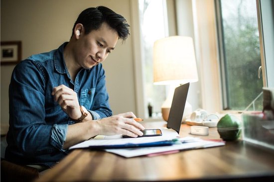 Man werkt aan bureau met witte Belkin oordopjes in, kijkt naar telefoon.