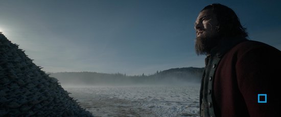 Leonardo DiCaprio met baard, in winterse kleding, kijkt uit over een besneeuwd landschap met mist.