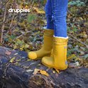 Een meisje in spijkerbroek, staand op een boomstam, draagt gele gevoerde regenlaarzen.