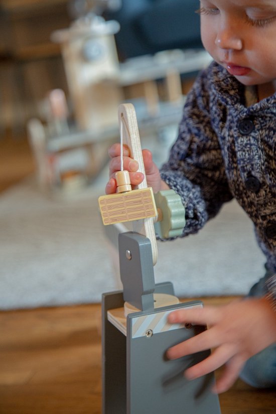 Detail van een houten kraan met een grijze basis en een houten arm, bespeeld door een kinderhand.