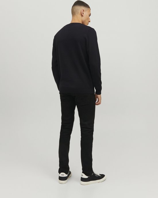 Een man staat met zijn rug naar de camera, gekleed in een zwarte trui en zwarte jeans.