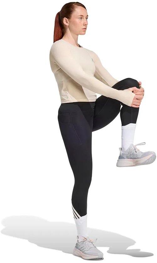 Vrouw in een beige longsleeve shirt en zwarte legging met driestrepen op de enkel.