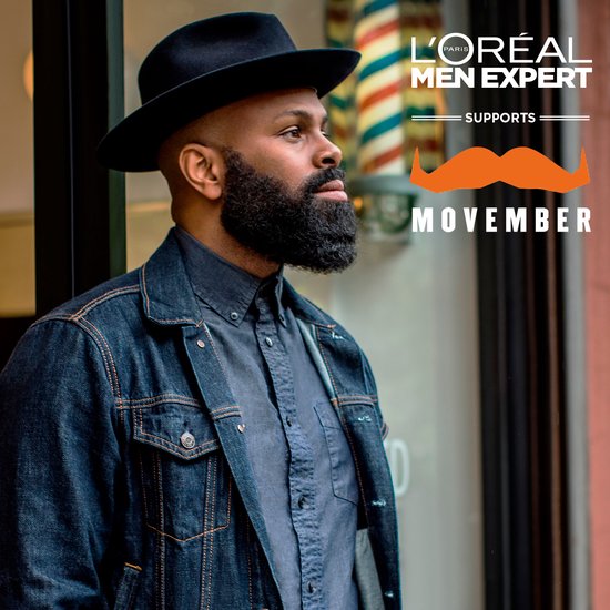 Man met baard en hoed voor kapperspaal, L'Oréal Men Expert Movember oranje snor logo.