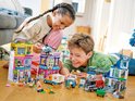 Twee kinderen spelen met LEGO City speelgoed, waaronder een politiegebouw en kleurrijke winkels.
