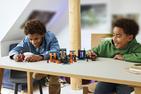 Deux garçons jouent avec un set LEGO Minecraft Wither Battle avec figurines et blocs de construction orange et gris.