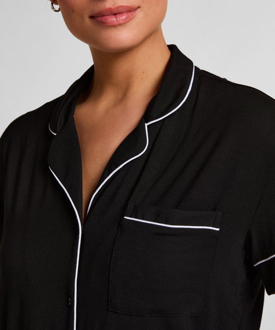 Close-up van een zwart pyjamashirt met korte mouwen, witte piping en een borstzakje.