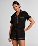 Vrouw in zwart pyjamashirt met witte bies en pyjamashort met koord.