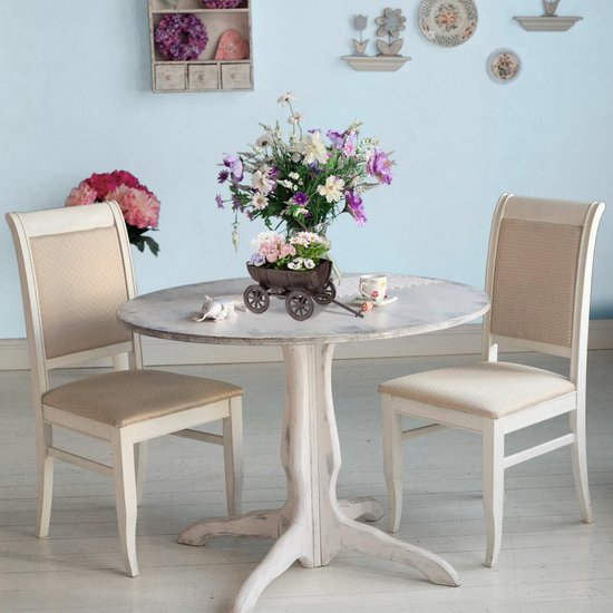 Bruin metalen wagentje met bloemen op een ronde tafel met twee stoelen.