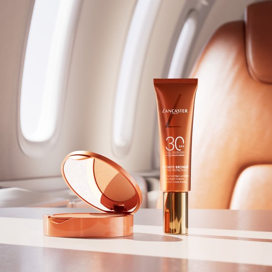 Lancaster Infinite Bronze getinte zonnebrandcrème tube en compact poeder op een vliegtuigtapijt.