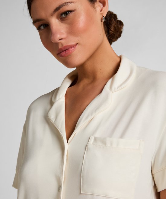 Close-up van een model in een gebroken witte pyjamashirt met borstzakje en kraag.