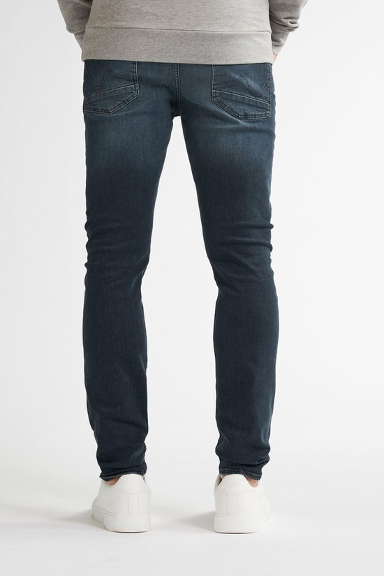 Man in grijze sweater en donkerblauwe jeans, staand, van achteren.