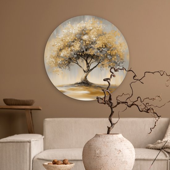 Ronde muurcirkel van een abstracte boom met gouden en grijze bladeren, in een bruin getinte woonkamer met een bank.