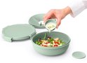 Main ajoutant de la vinaigrette à une boîte à salade vert pâle avec salade, un couvercle et un diviseur.