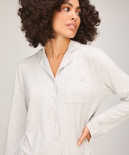 Model draagt lichtgrijs pyjamashirt met reverskraag, knoopsluiting en borstzak, zijaanzicht.