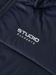 Close-up van Studio Outdoors logo op een donkerblauwe, gewatteerde jas.