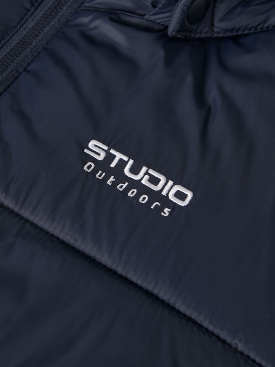 Close-up van Studio Outdoors logo op een donkerblauwe, gewatteerde jas.