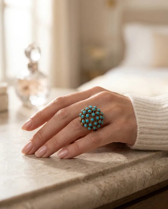 Vintage bronzen ring met turquoise kralen in een bolvorm, gedragen aan de vinger van een model.