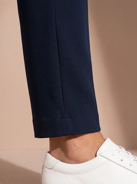 Detail van de zoom van een donkerblauwe sportbroek met witte stiksels, gedragen met witte sneakers.